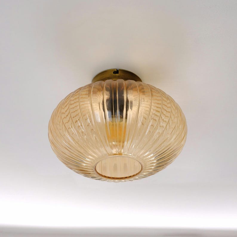 May include: A ceiling light fixture with a round, ribbed, amber glass shade and a brass base.