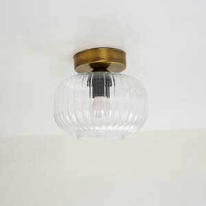 Op de afbeelding: Een plafondlamp van helder glas met een geribbeld ontwerp en een messing afwerking.
