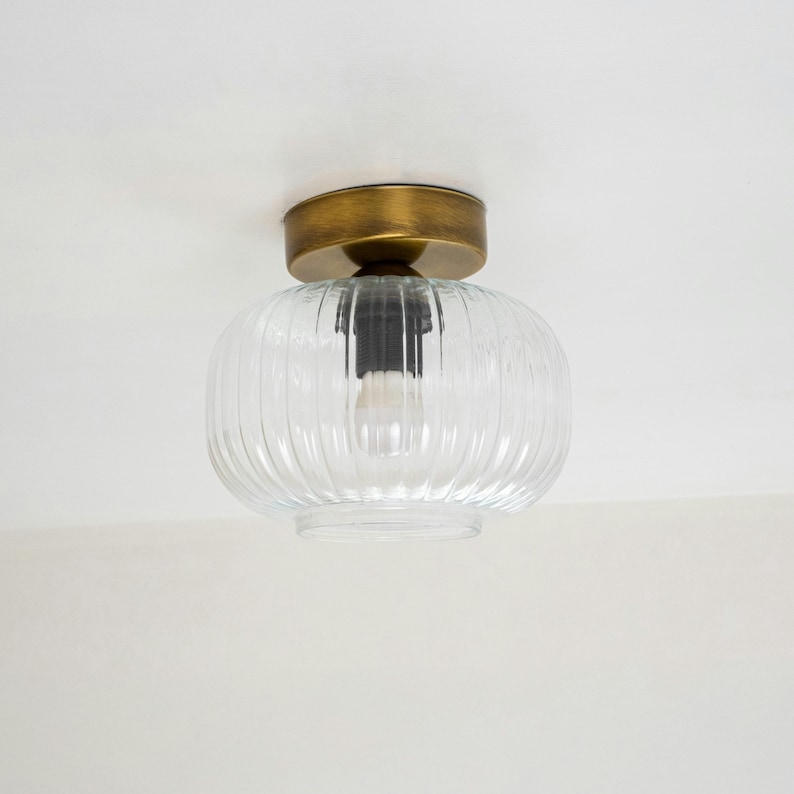 Op de afbeelding: Een plafondlamp van helder glas met een geribbeld ontwerp en een messing afwerking.