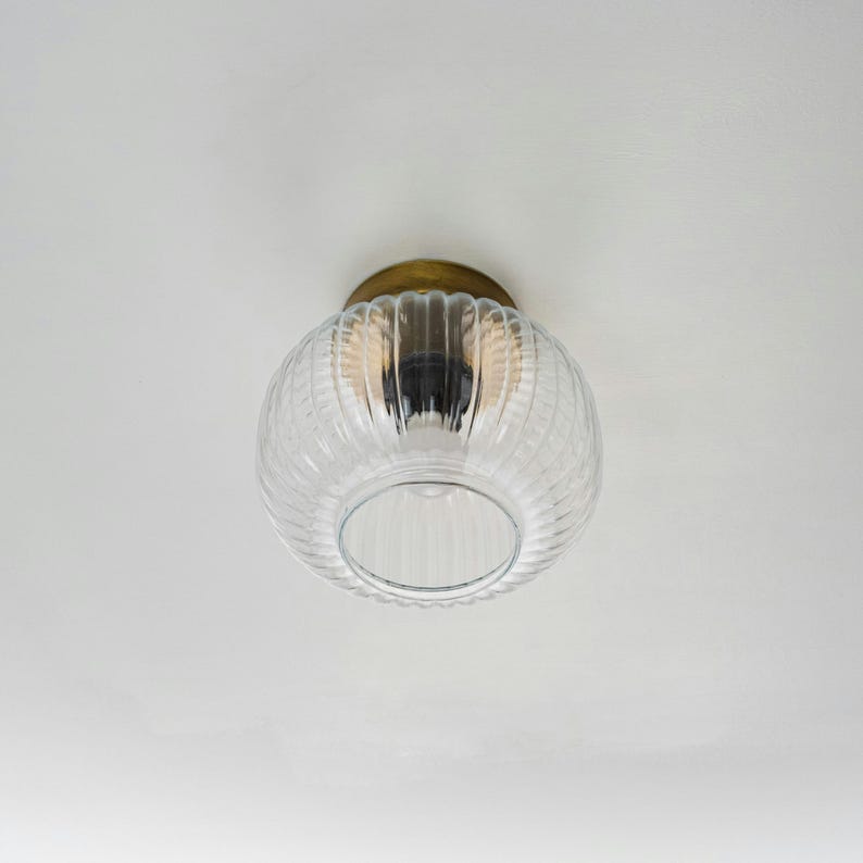 Op de afbeelding: Een plafondlamp van helder glas met een geribbeld ontwerp en een messing afwerking.