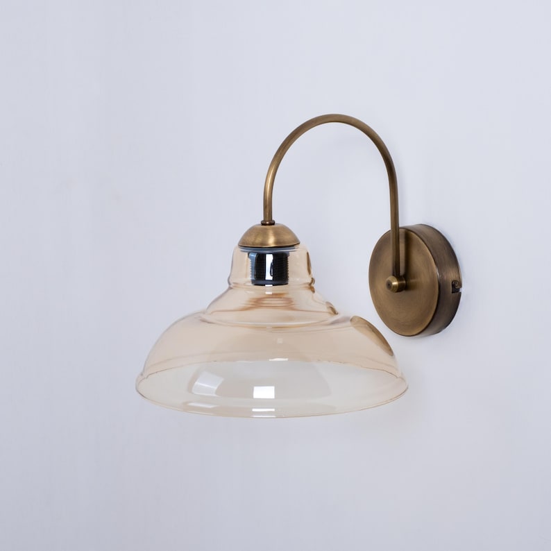 May include: A brass wall sconce with a curved arm and a amber glass shade.