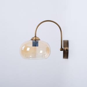 May include: A brass wall sconce with a curved arm and a round amber glass shade.