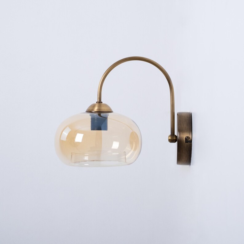 May include: A brass wall sconce with a curved arm and a round amber glass shade.