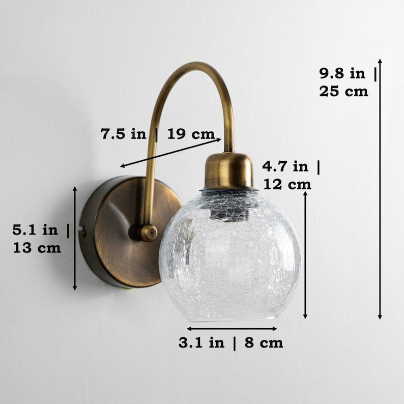 K&ouml;nnte beinhalten: Eine Wandleuchte aus Messing mit einem klaren Glaskugelschirm. Der Schirm hat eine craquel&eacute;e Textur. Die Leuchte ist 25 cm hoch, 19 cm breit und 13 cm tief.