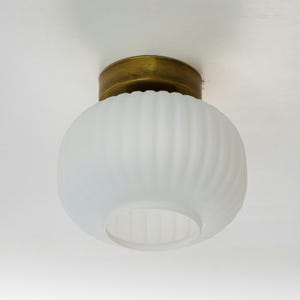 Op de afbeelding: Een witte, gematteerde glazen plafondlamp met een messing rand. Het glas heeft een geribbeld ontwerp.