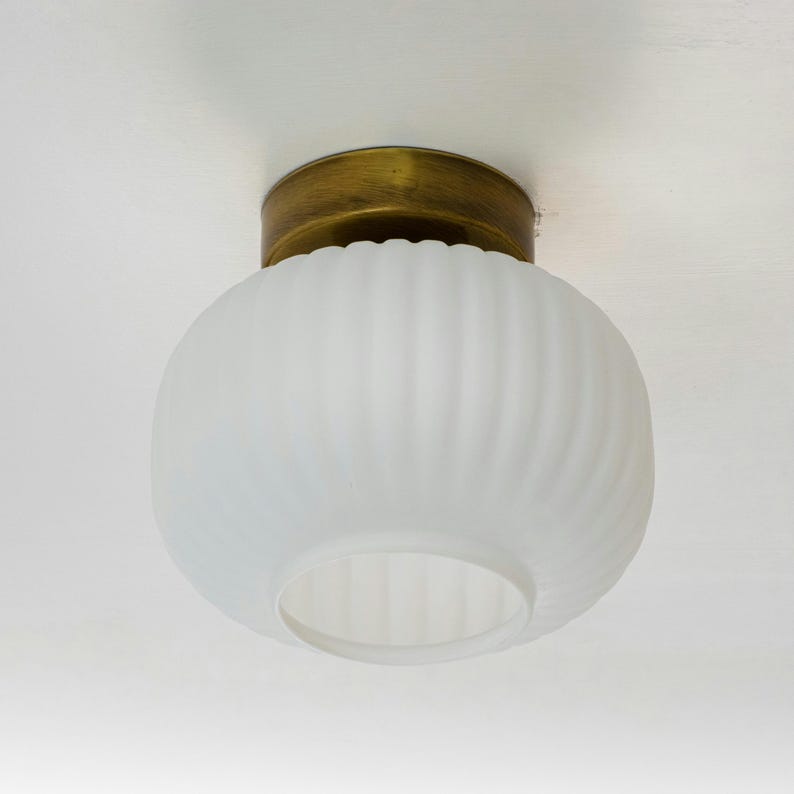 Op de afbeelding: Een witte, gematteerde glazen plafondlamp met een messing rand. Het glas heeft een geribbeld ontwerp.