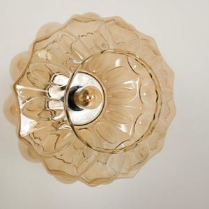 May include: A decorative, amber-colored glass ceiling light fixture. The light has a scalloped, flower-like design around the edges and a circular center with a visible lightbulb. The fixture is designed to be mounted on a ceiling.