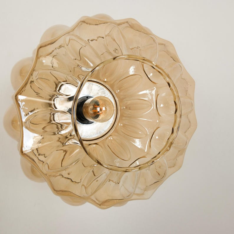 May include: A decorative, amber-colored glass ceiling light fixture. The light has a scalloped, flower-like design around the edges and a circular center with a visible lightbulb. The fixture is designed to be mounted on a ceiling.