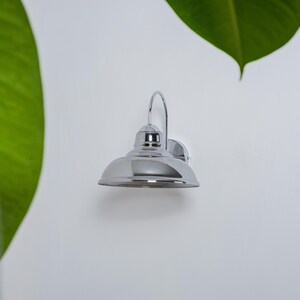 May include: A chrome wall sconce with a bell-shaped shade. The sconce is mounted on a white wall.