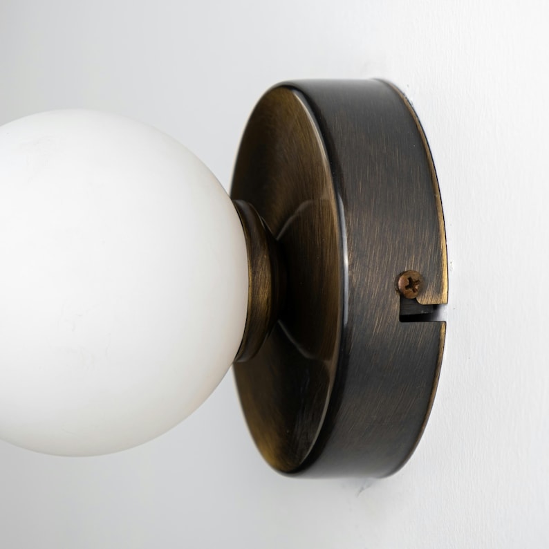 Op de afbeelding: Een close-up van een wandlamp met een witte, matte glazen bol en een basis van geborsteld messing.