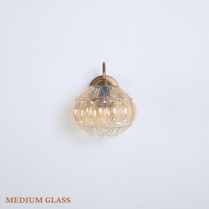 Puede incluir: Aplique de pared de cristal &aacute;mbar de tama&ntilde;o mediano con un dise&ntilde;o decorativo. Tiene una placa de montaje de metal color lat&oacute;n y un brazo curvo. El texto "MEDIUM GLASS" est&aacute; en la parte inferior de la imagen.