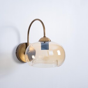 May include: A brass wall sconce with a curved arm and a round amber glass shade.