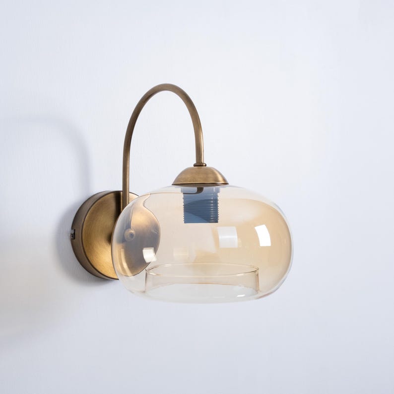 May include: A brass wall sconce with a curved arm and a round amber glass shade.