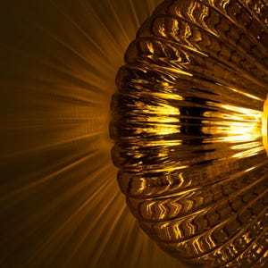 May include: A gold-toned glass lampshade with a ribbed texture. The lampshade is lit and casting a warm glow.