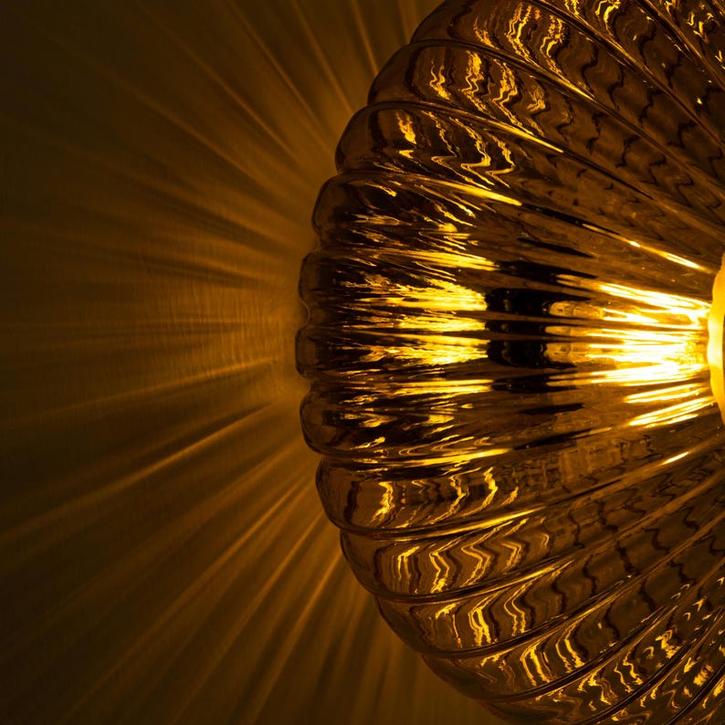 May include: A gold-toned glass lampshade with a ribbed texture. The lampshade is lit and casting a warm glow.