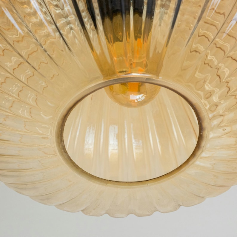 May include: Close-up of a light brown glass lampshade with a ribbed texture. The lampshade has a round opening at the top, revealing a light bulb.