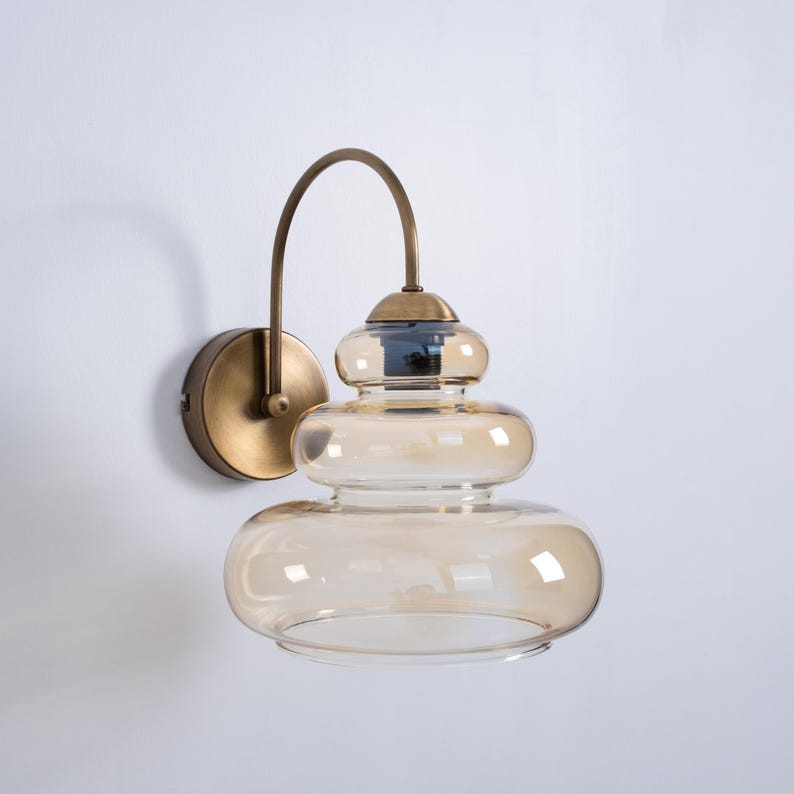 May include: A brass wall sconce with a layered amber glass shade. The sconce has a curved arm and a round base.