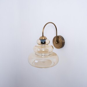May include: A brass wall sconce with a curved arm and a layered amber glass shade.