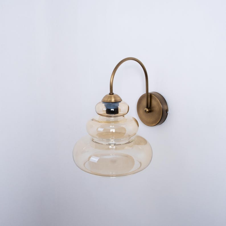May include: A brass wall sconce with a curved arm and a layered amber glass shade.