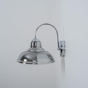 May include: A chrome wall sconce with a curved arm and a round, reflective shade.