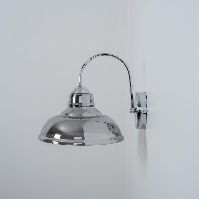 May include: A chrome wall sconce with a curved arm and a round, reflective shade.