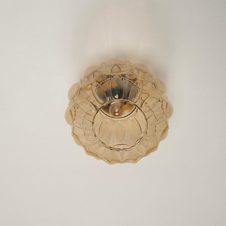 May include: A vintage-style, amber-colored glass ceiling light fixture. The light has a floral design and a round shape. The fixture is mounted on a white ceiling. The light bulb is visible inside the fixture.