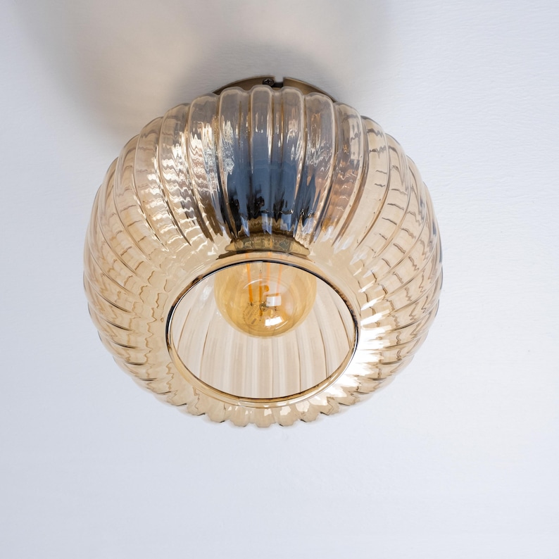 May include: A brown glass ceiling light fixture with a ribbed design. The light is on and the bulb is visible.