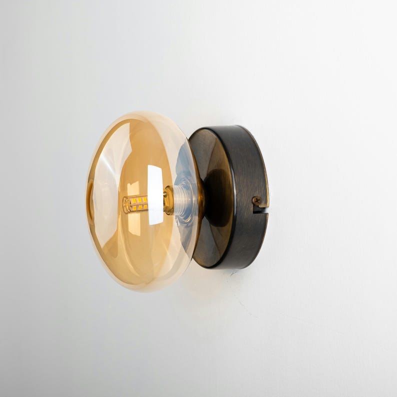 May include: A wall-mounted light fixture with a round, amber glass shade and a black metal base.