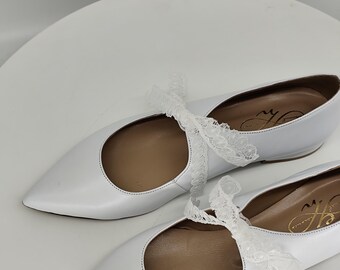 May include: A pair of white leather ballet flats with lace ties. The flats have a pointed toe and a low heel.