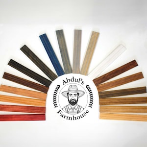 May include: A fan-shaped display of 15 wood stain samples, each a different color, ranging from light to dark. The samples are arranged in a semi-circle with the darkest stain at the bottom and the lightest stain at the top. The samples are labeled with the name "Abdul's Farmhouse".