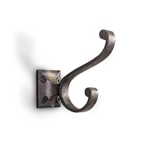 May include: A wrought iron wall hook with a dark, textured finish. The hook features a square mounting plate with four screws and a curved, double-ended hook design. The hook is designed for hanging items.