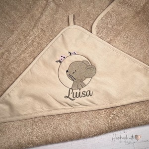 Puede incluir: Una toalla con capucha beige con un rat&oacute;n bordado marr&oacute;n y el nombre "Luisa" en ella. El rat&oacute;n est&aacute; rodeado de tres mariquitas rosas. La toalla tiene el texto "Handmade with love by Tanja" en la esquina inferior derecha.