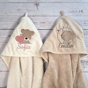 Puede incluir: Dos toallas con capucha con dise&ntilde;os bordados. Una toalla presenta un oso marr&oacute;n sosteniendo un coraz&oacute;n rosa con el nombre "Sofia" bordado debajo. La otra toalla presenta un rat&oacute;n marr&oacute;n con acentos de mariposas rosas y el nombre "Emilia" bordado debajo.