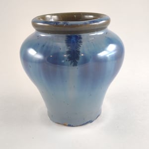 May include: A small, blue and white ceramic vase with a brown rim. The vase has a slightly rounded body and a narrow opening.
