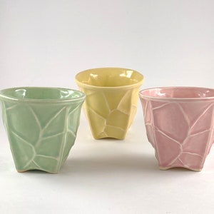 May include: Three ceramic cups in green, yellow, and pink. Each cup has a geometric, textured design.