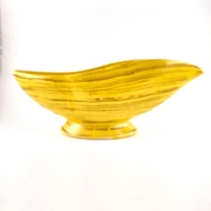 May include: A yellow ceramic bowl with a wavy, leaf-like shape and a striped pattern. The bowl has a small, round base.