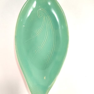 May include: A light green ceramic serving dish shaped like a leaf with a swirl design.