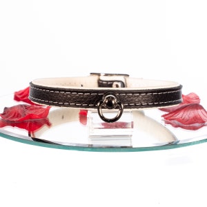 May include: A black leather collar with white stitching and a silver ring.