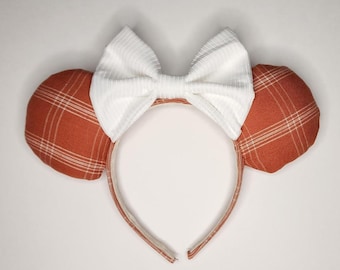 May include: A pair of orange and white plaid Minnie Mouse ears with a white bow.