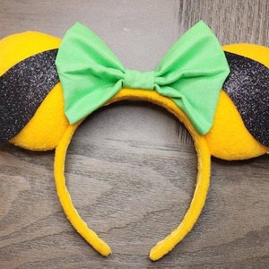 May include: Yellow and black mouse ears with a green bow. The ears are fuzzy and have black glitter accents. The bow is made of fabric.