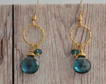 May include: Gold hoop earrings with a dangling blue topaz gemstone and smaller blue topaz accents.