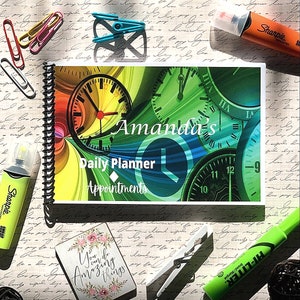 May include: A colorful daily planner with a spiral binding and a cover featuring a design of clocks with the text "Amanda's Daily Planner Appointments".