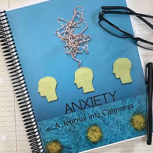 Può includere: Un diario blu con il titolo "Ansia: Un diario per la calma". La copertina presenta tre teste di feltro giallo con uno spago rosso e bianco aggrovigliato collegato alla testa superiore.