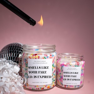 May include: Two candles with colorful sprinkles on the sides. The larger candle is 8 oz and says "Smells like your fake I.D. is expired". The smaller candle is 4 oz and says "Smells like your fake I.D. is expired".