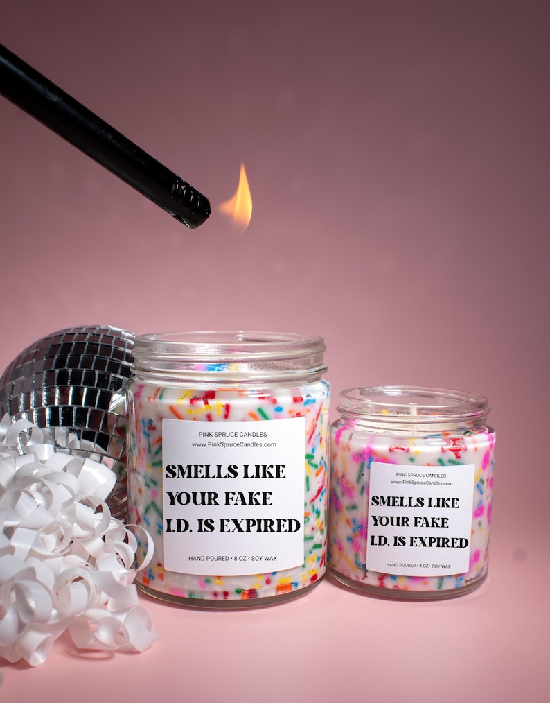 May include: Two candles with colorful sprinkles on the sides. The larger candle is 8 oz and says "Smells like your fake I.D. is expired". The smaller candle is 4 oz and says "Smells like your fake I.D. is expired".