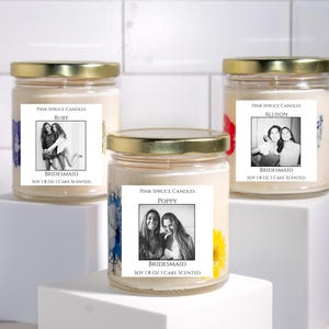 Może przedstawiać: Trzy świece w szklanych słoikach ze złotymi nakrętkami, wypełnione kremowym woskiem sojowym. Etykiety zawierają tekst Pink Spruce Candles, imiona Ruby, Allison lub Poppy, słowo Bridesmaid oraz Soy 18 Oz I Cake Scented wraz z czarno-białymi zdjęciami.