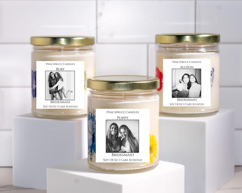 Może przedstawiać: Trzy świece w szklanych słoikach ze złotymi nakrętkami, wypełnione kremowym woskiem sojowym. Etykiety zawierają tekst Pink Spruce Candles, imiona Ruby, Allison lub Poppy, słowo Bridesmaid oraz Soy 18 Oz I Cake Scented wraz z czarno-białymi zdjęciami.