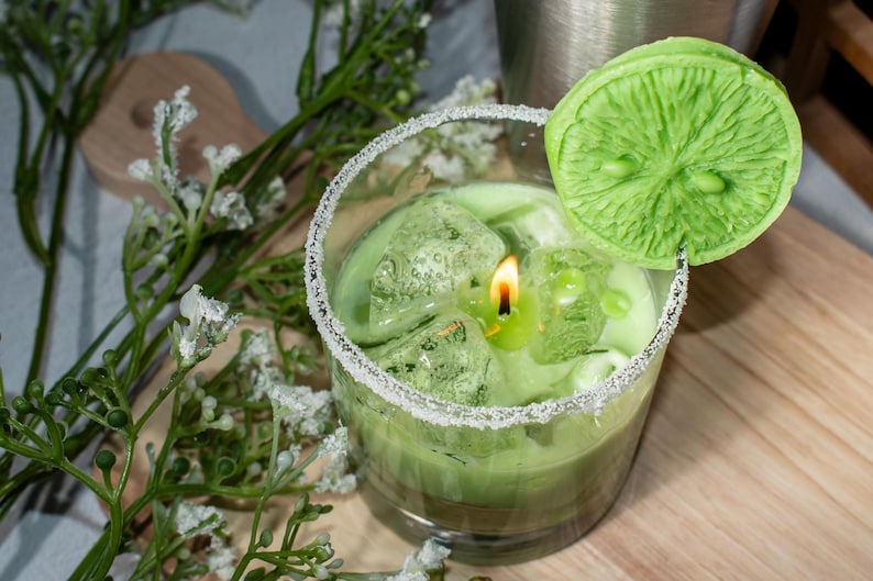 May include: A green candle in a glass jar with a sugared rim. The candle is topped with a green lime slice and ice cubes.
