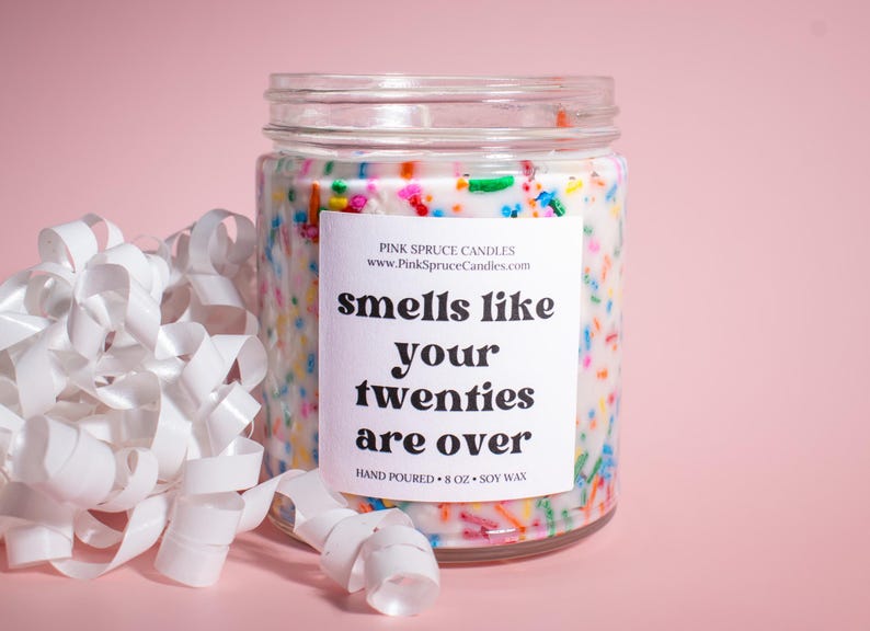 May include: A white candle jar with a colorful sprinkle design and a label that reads "smells like your twenties are over". The candle is hand-poured and made with soy wax.
