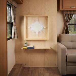 Op de afbeelding: Een houten kompasroos met LED-verlichting, gemonteerd op een muur in een vierkant frame. Daaronder een kleine plank met een plant en boeken. Het interieur heeft houten panelen en een raam met geruite gordijnen.